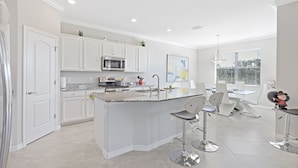 A modern kitchen with white cabinets, a central island, and bar stools. - Modern Waterfront Home in Artesia | Pool/Gym (Naples)