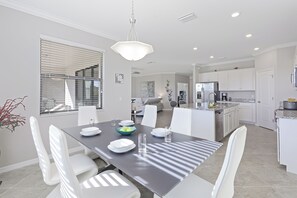 A modern kitchen with white cabinets, a stainless steel refrigerator, and a dining area with a dark table and white chairs.
