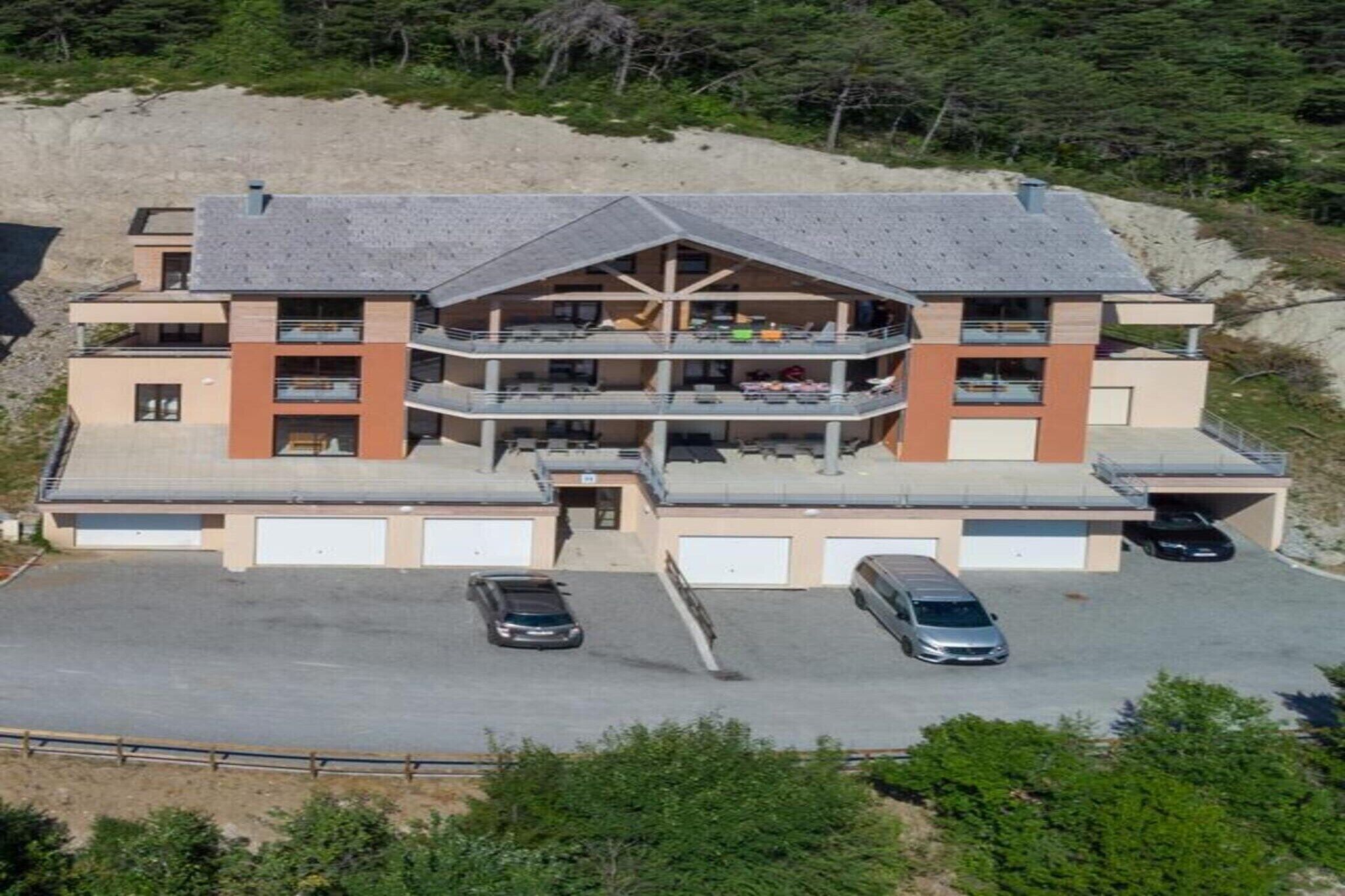 Un immeuble à plusieurs étages doté d’un atrium central, de nombreux balcons et d’un espace de stationnement pouvant accueillir deux voitures.