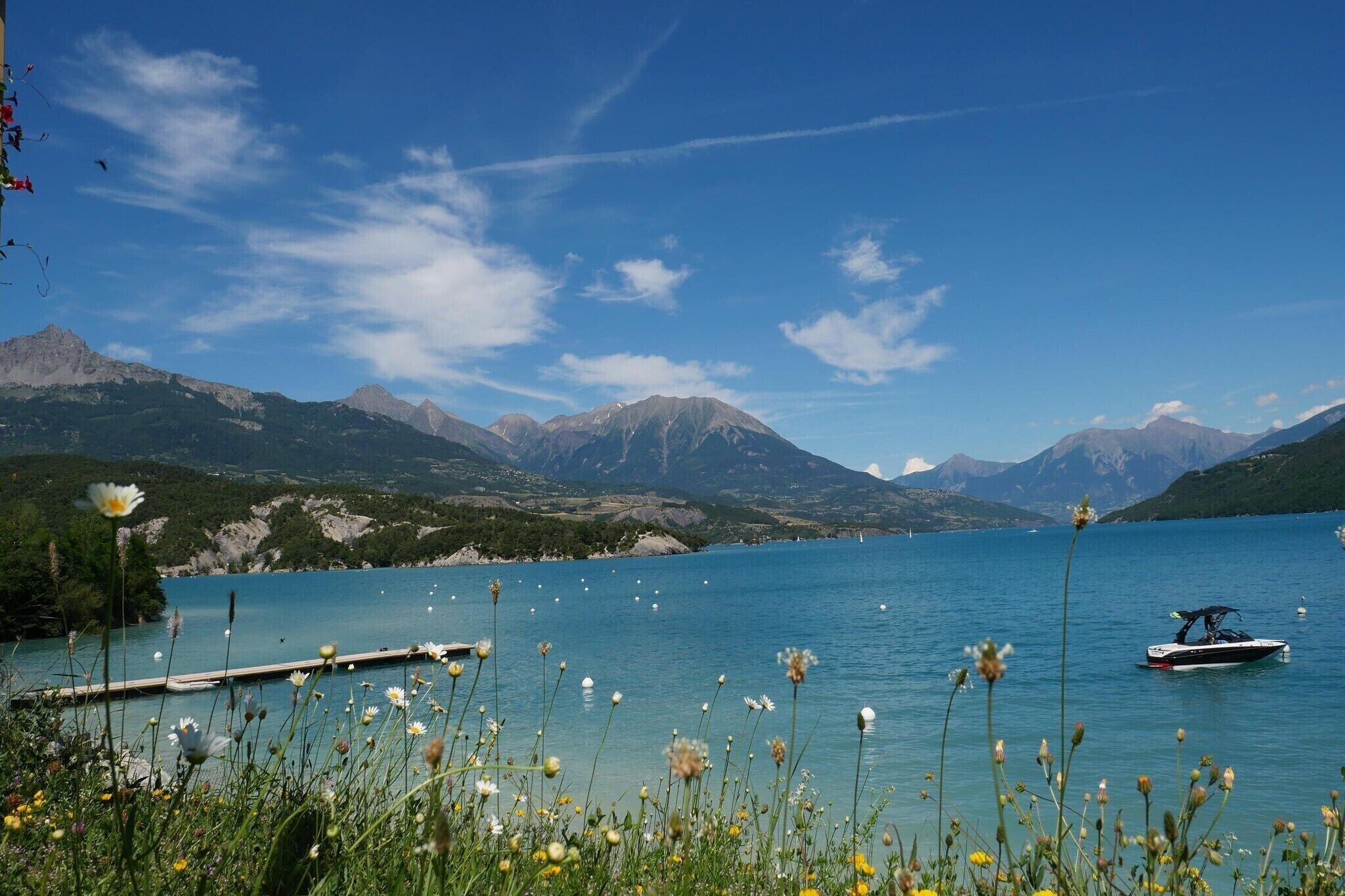 Un lac paisible, avec des montagnes en arrière-plan, un quai et un bateau.