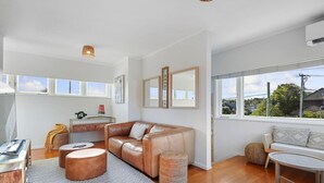 Un salon moderne avec un canapé en cuir, une table basse et une table ronde. De grandes fenêtres offrent une vue sur l’extérieur.