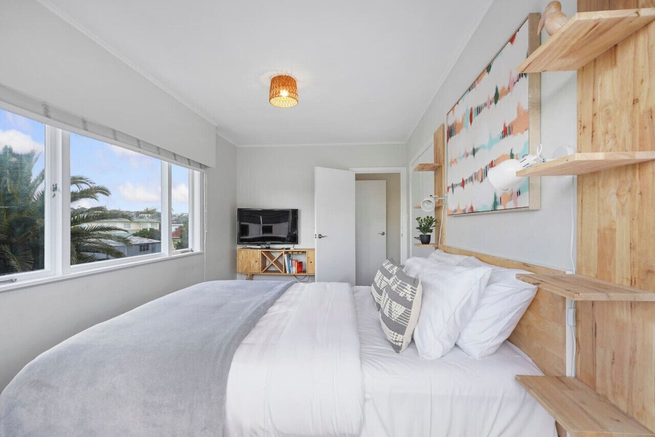A modern bedroom with a large bed, a television, and wooden shelves with artwork.