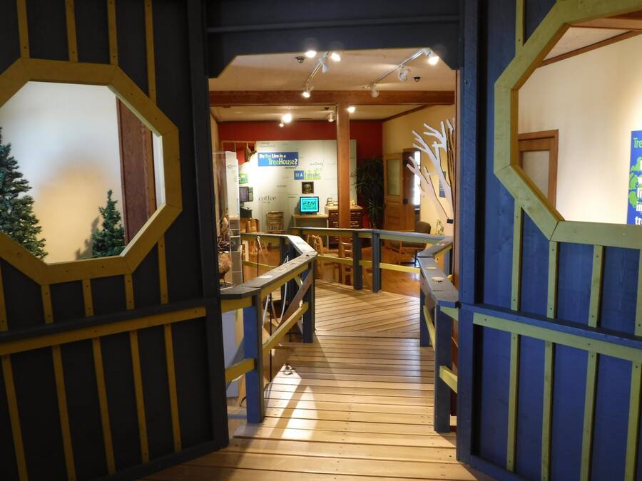 A wooden interior with a staircase leading to a room with a computer and a sign that reads "Do You Live in a Treehouse?"