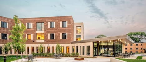 A modern building with a brick facade, multiple windows, and a covered outdoor seating area with tables and chairs.