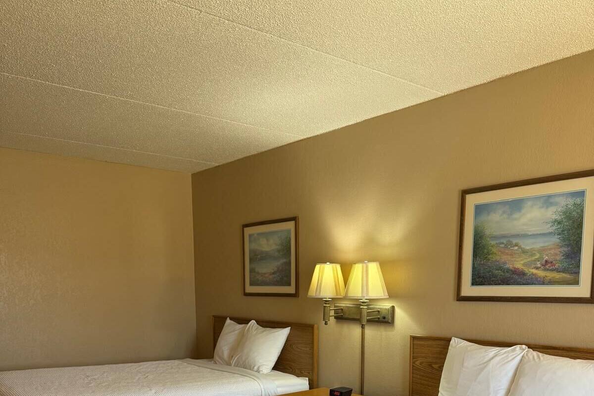 A hotel room with two beds, a nightstand with a lamp, and two framed pictures on the wall.