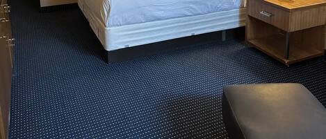 Ein Hotelzimmer mit Bett, Nachttisch mit Lampe, Bank und einer Tür zu einem weiteren Raum.