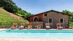 Ein Poolbereich mit Liegestühlen und einem Steinhaus mit Bogenfenstern.