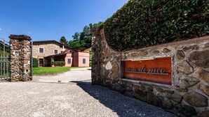 Eine Steinsmauer mit einem Schild, auf dem "casa du meo" steht, und ein Schotterweg, der zu einem Gebäude mit roter Fassade und Steinmauern führt.