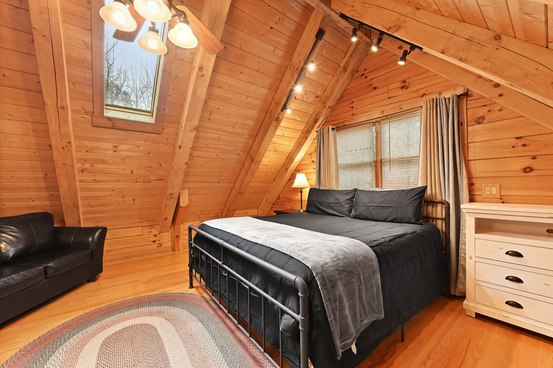 A cozy attic bedroom with a bed, a chair, a dresser, and a window with curtains.