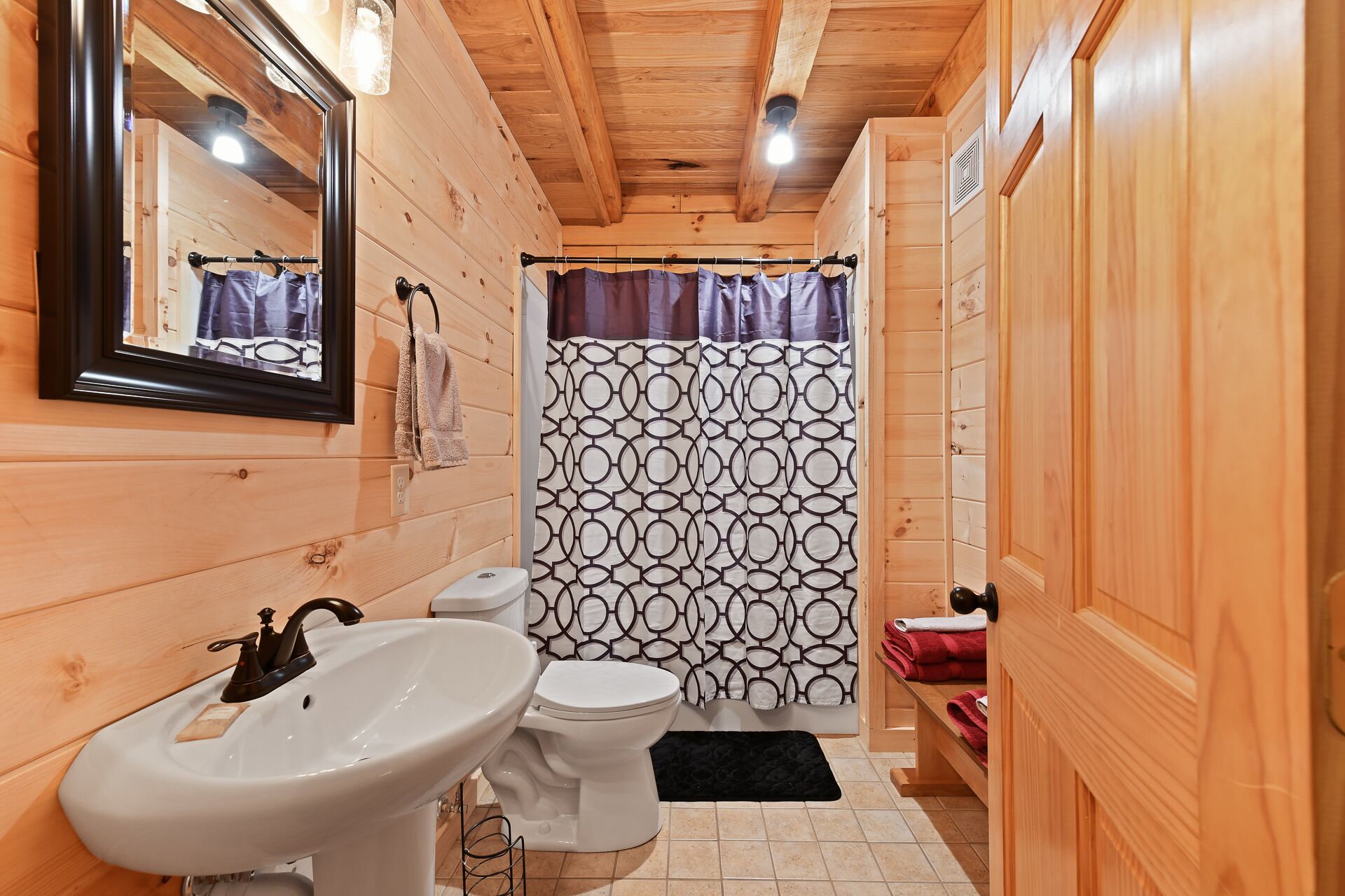 Une salle de bain rustique, avec des murs en bois, comprenant un lavabo, des toilettes et un rideau de douche.