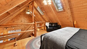 A cozy attic bedroom with a wooden ceiling, a bed, a black leather chair, and a small window. - Cabin In Hocking Hills! Pet Friendly, Hot Tub, Secluded. (Logan)