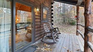 A log cabin with a porch, two rocking chairs, and a glass door leading to a dining area. - Cabin In Hocking Hills! Pet Friendly, Hot Tub, Secluded. (Logan)