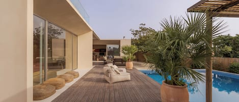 A modern outdoor deck with a pool, lounge chairs, and potted plants.