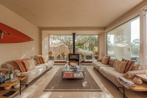 Uma sala de estar moderna com uma mesa de centro de vidro, dois sofás, uma lareira e janelas amplas.