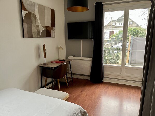 Ein Schlafzimmer mit Bett, Schreibtisch mit Lampe, Fernseher und einem Fenster mit Vorhängen.
