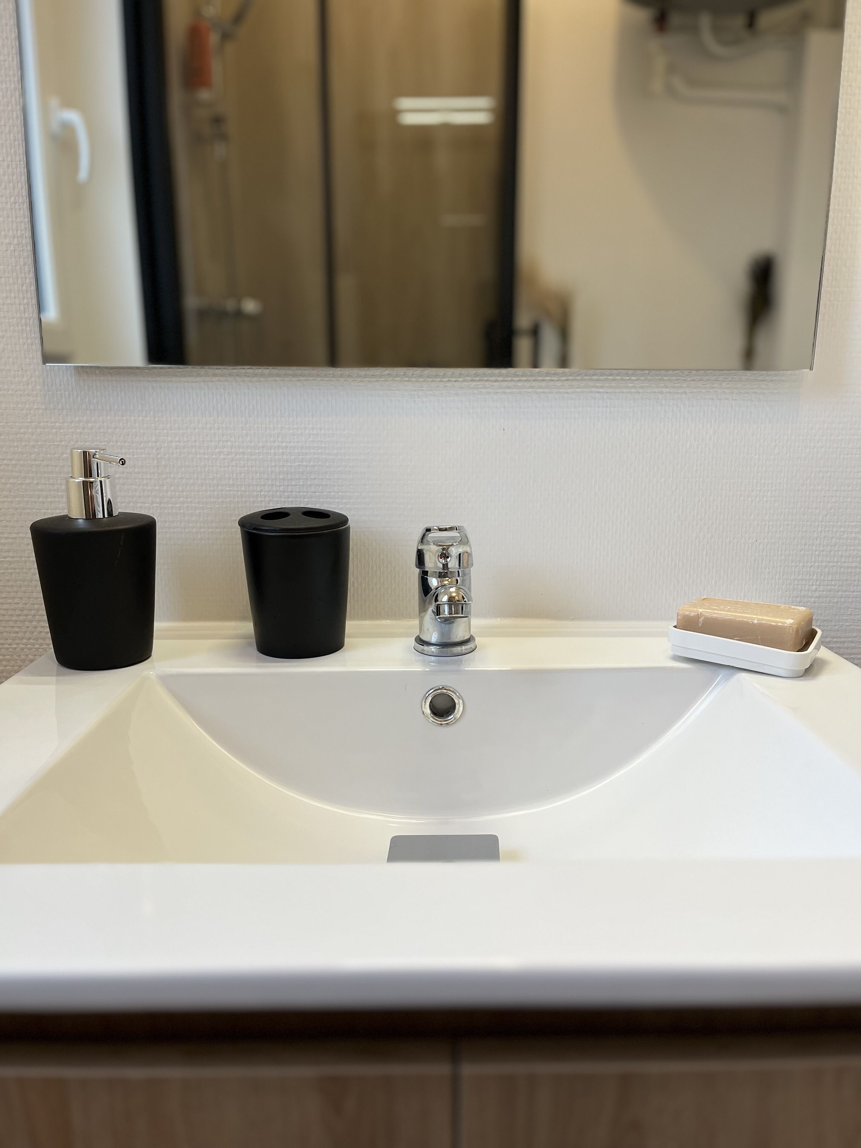 A bathroom sink with a mirror above it, a soap bar, and two black containers.