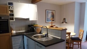 Une cuisine compacte équipée d’un évier, de meubles en bois et d’un petit coin repas avec une chaise et une table.