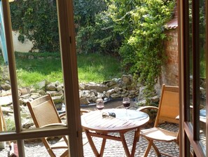Un patio al aire libre con una mesa redonda y dos sillas de mimbre, una copa de vino tinto y un par de gafas de sol sobre la mesa.