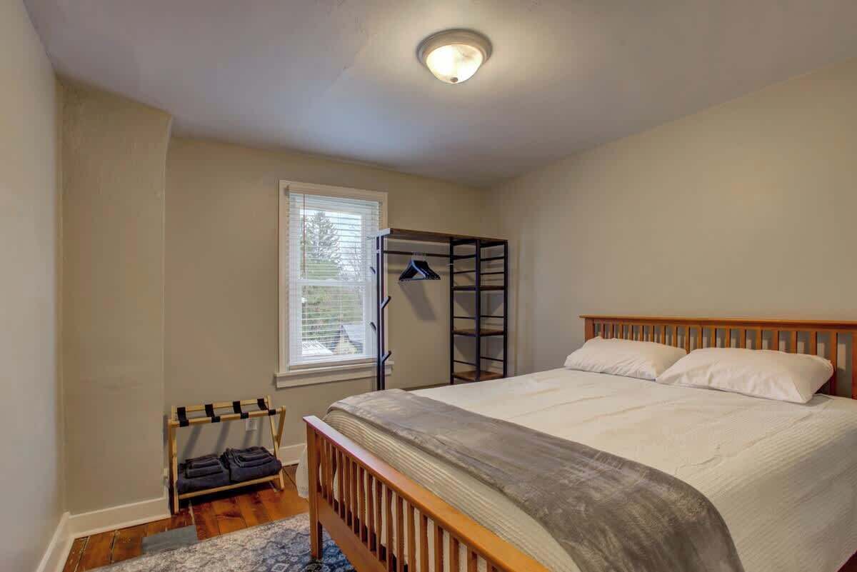 Quarto com cama, janela, um banco de madeira e luminária no teto.