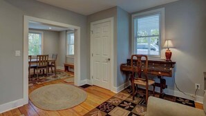 Una habitación con piso de madera, un tapete redondo, un escritorio con lámpara y una silla.