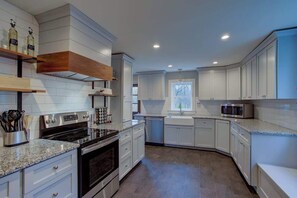 Una cocina moderna con armarios blancos, horno empotrado, microondas y ventana que deja entrar luz natural.