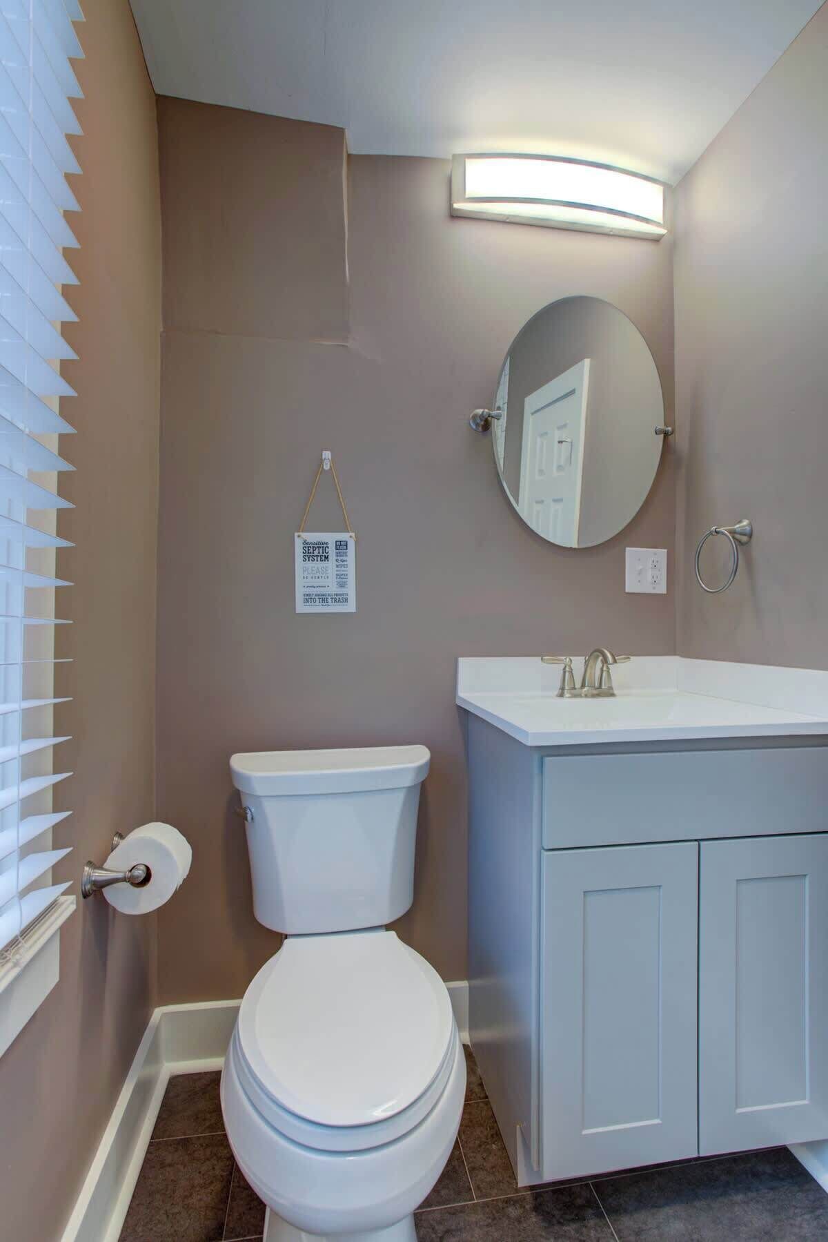 A bathroom with a toilet, sink, mirror, and a sign indicating a septic system.