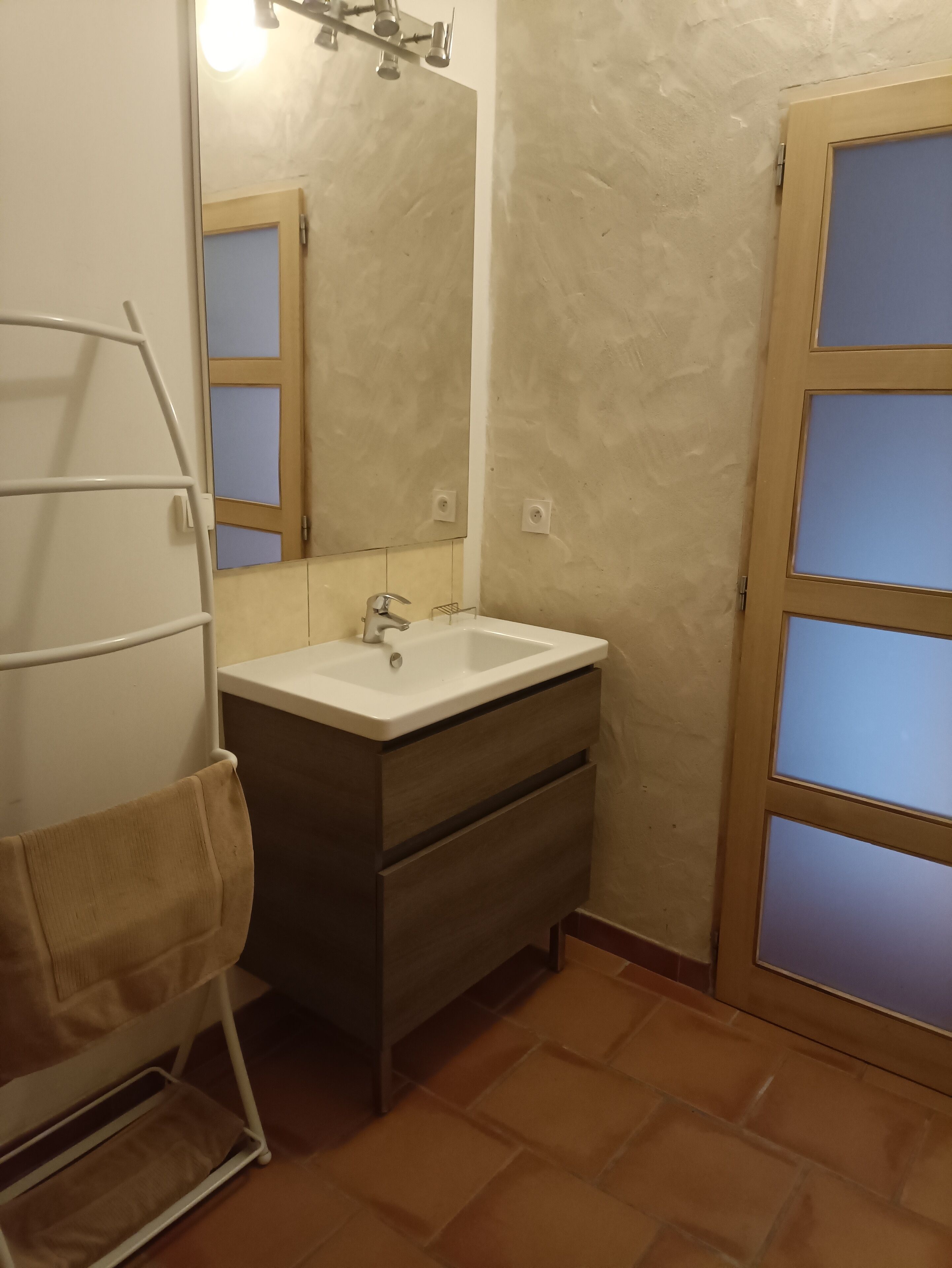 A bathroom with a white sink, wooden vanity, and a towel rack.