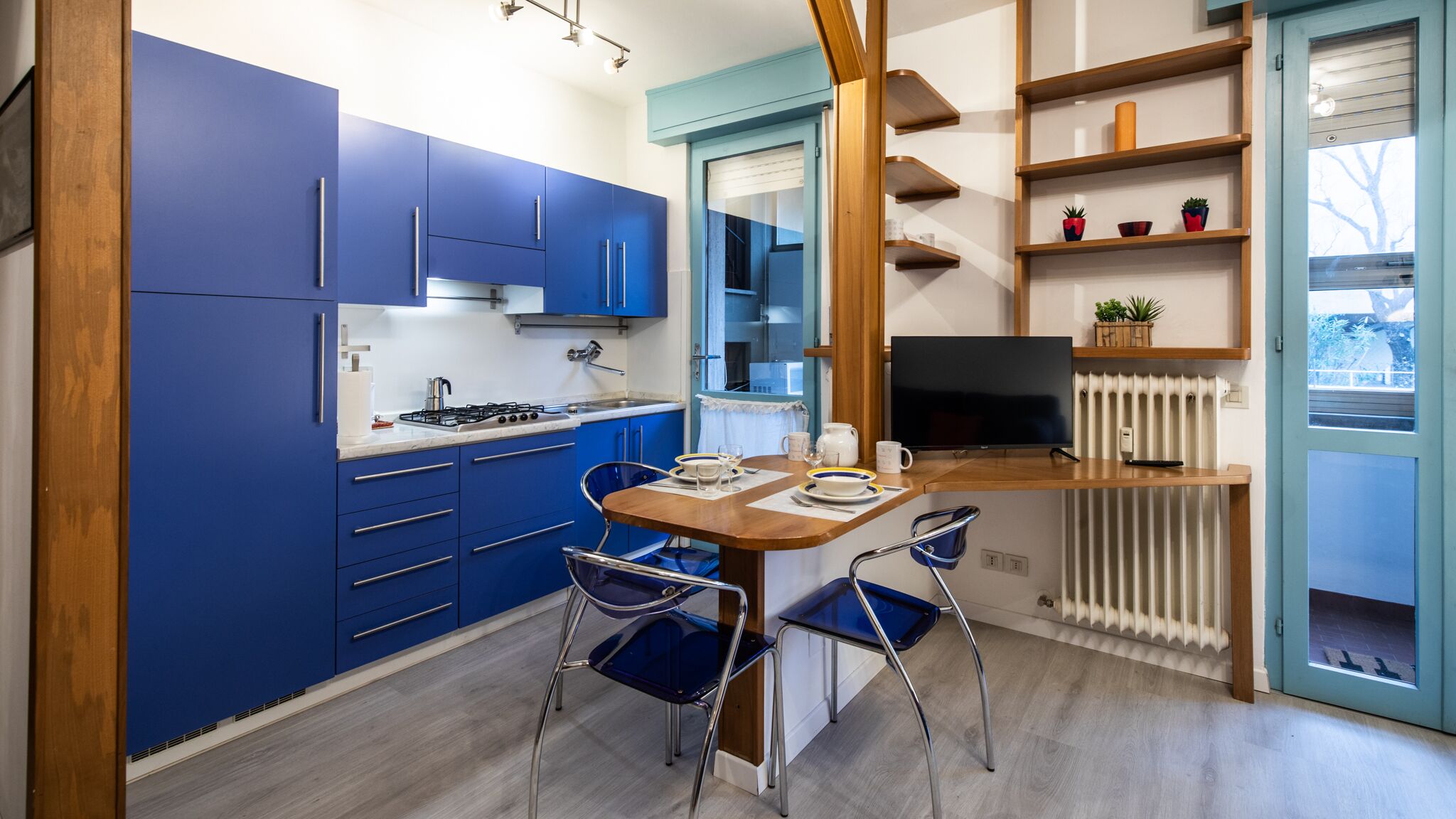 A compact kitchen with blue cabinets, a wooden dining table, and two chairs.