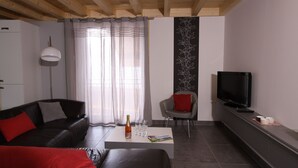 Een moderne woonkamer met een zwarte leren bank, een rode plaid, een witte salontafel, een televisie en een decoratief wandpaneel.