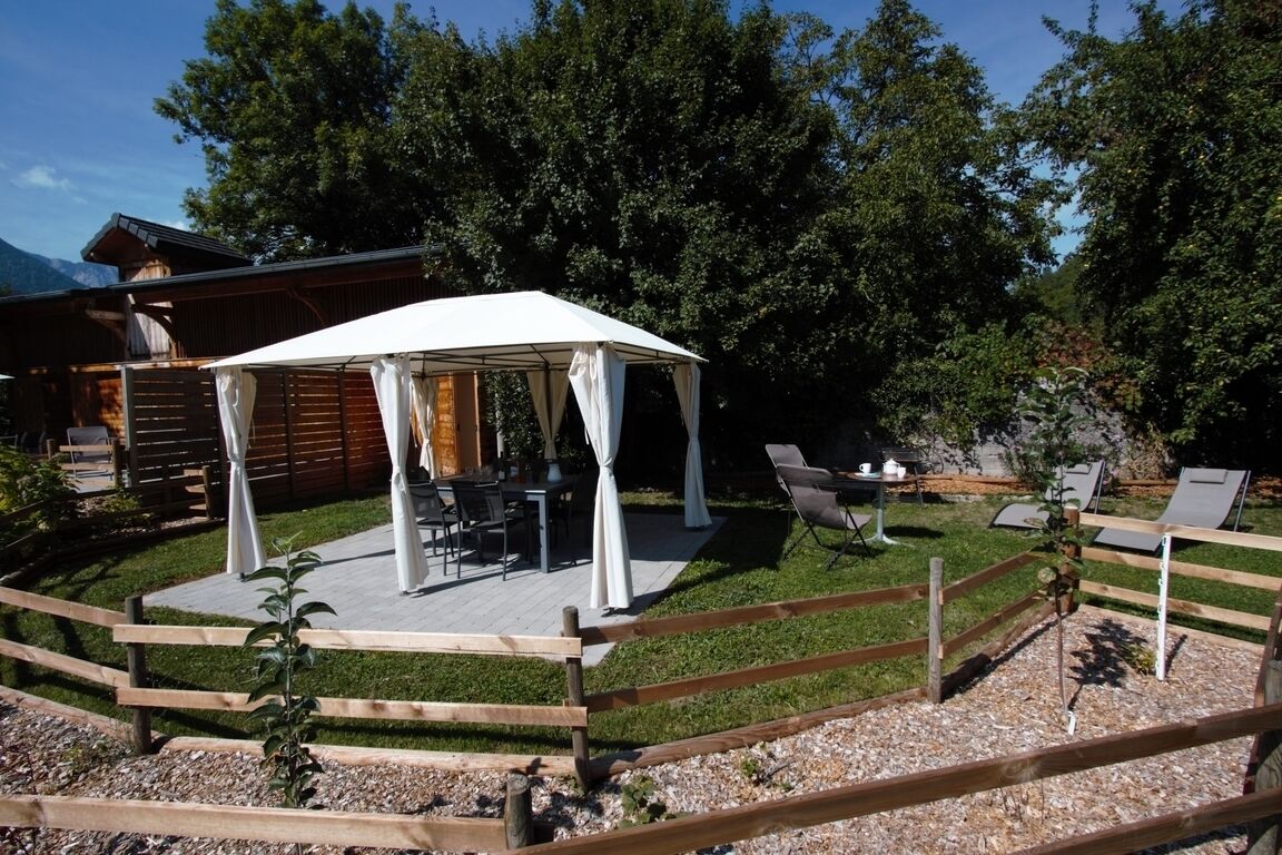Une terrasse en bois surmontée d’un auvent blanc, dotée de mobilier d’extérieur et d’un espace clos avec des chaises longues.