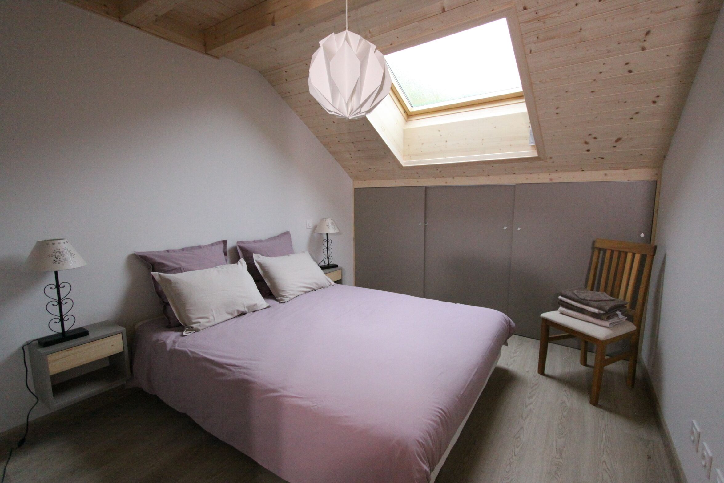 A bedroom with a bed, nightstands, a chair, and a skylight.
