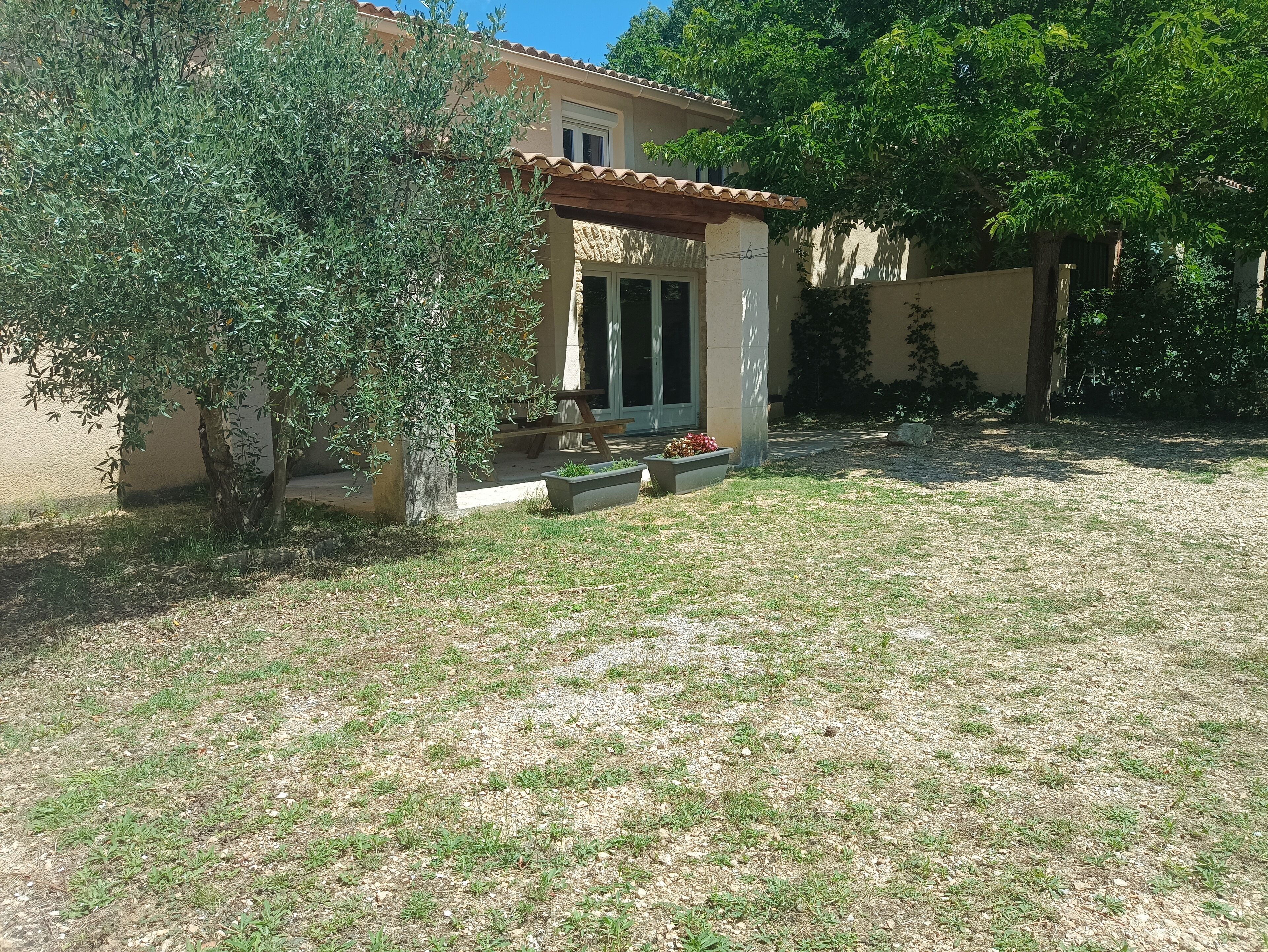 Una casa con techo de tejas, un pequeño porche y un jardín con césped y un árbol.