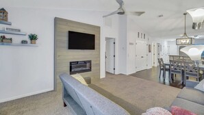 Ein modernes Wohnzimmer mit Flachbildfernseher, Kamin, Deckenventilator und Essbereich mit Tisch und Stühlen.