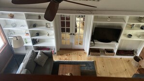 A room with a ceiling fan, a television on a shelf, and a sofa.