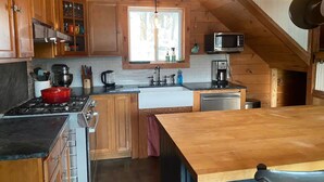 A compact kitchen with wooden cabinets, a stove, a microwave, and a large island.