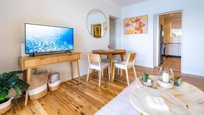 Una sala de estar moderna con una televisión de pantalla plana, muebles de madera, una mesa de comedor y una cocina visible a través de un arco.