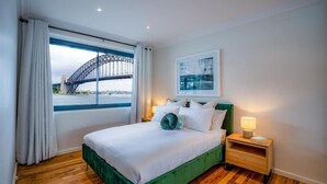 Una habitación de hotel con una cama, una mesita de noche, una ventana con vista a un puente y un cuadro en la pared.
