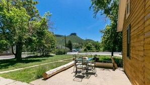 A patio area with a table and chairs, a wooden building, and a view of a hill.