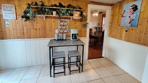 A room with a wooden wall, a table with two stools, a coffee machine, and a sign reading 'BACK IN 1952'.