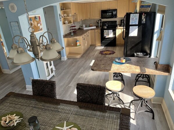 A modern kitchen with wooden cabinets, a black refrigerator, and a dining area with wicker furniture and a glass table.