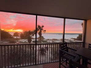 A balcony with a view of the beach and ocean during sunset.