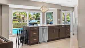 A modern kitchen with a large island, dark cabinetry, and a view of a pool and greenery.