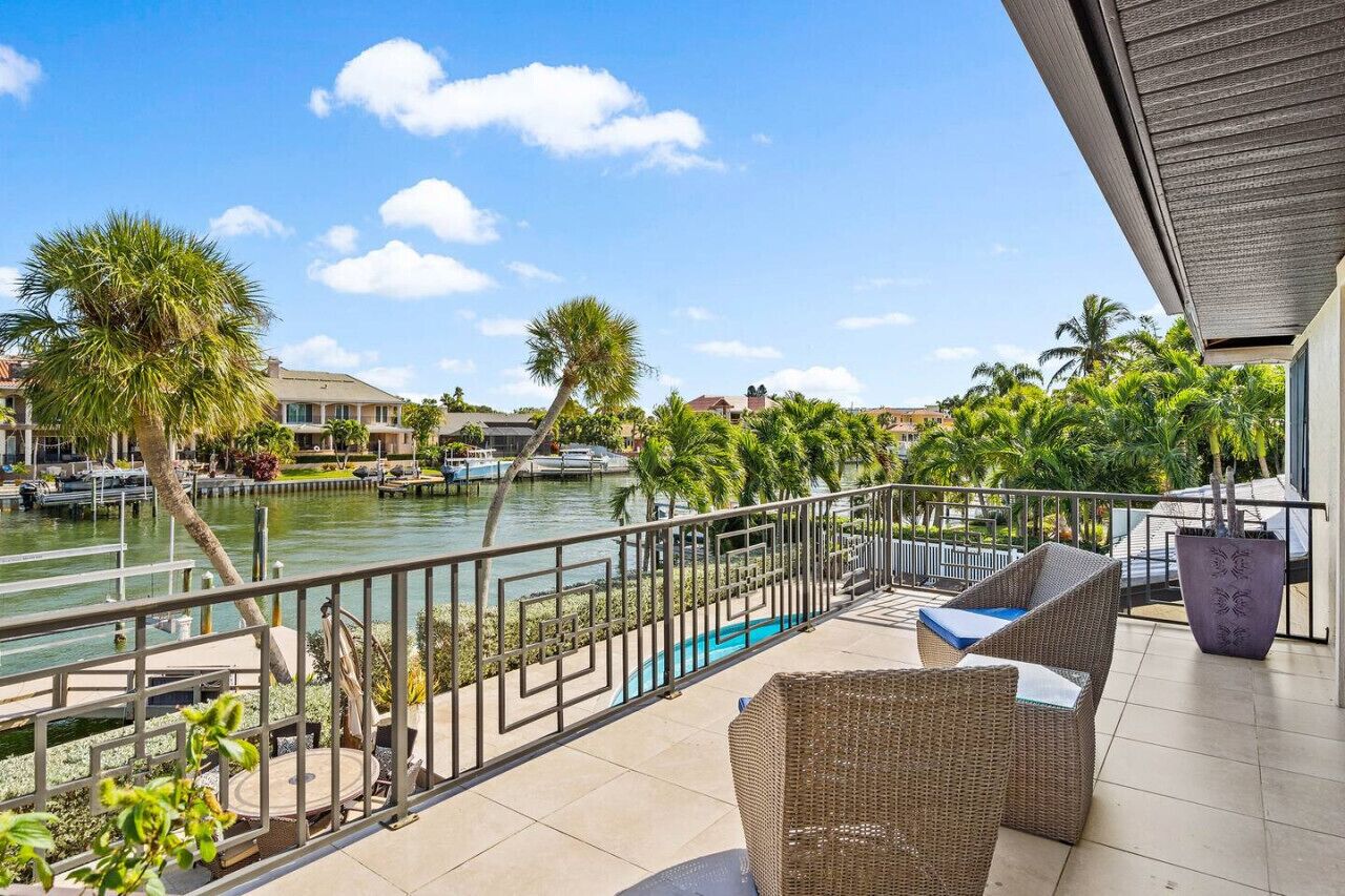 Een balkon met rieten meubilair, een zwembad en uitzicht op een jachthaven met boten en palmbomen.