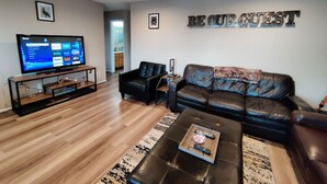 A modern living room with a leather sofa, a coffee table, and a flat-screen TV on a wooden stand. - Stylish Steampunk Home for Extended Stays (Denver)