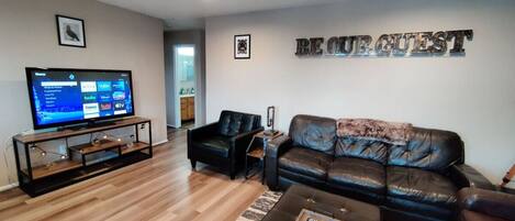 A modern living room with a leather sofa, a coffee table, and a flat-screen TV on a wooden stand.
