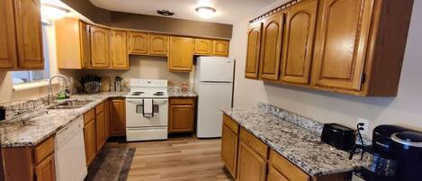 A kitchen with wooden cabinets, granite countertops, a stove, a refrigerator, and a coffee maker.