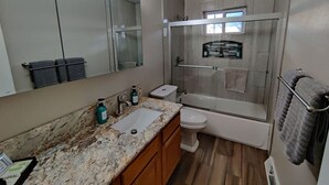 A modern bathroom with a granite countertop, a glass shower enclosure, and a toilet. - Stylish Steampunk Home for Extended Stays (Denver)