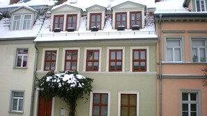 A multi-story building with a row of windows on the ground floor, a balcony with plants, and a snow-covered roof. - Apartment AltstadtErleben 2 (upper floor) (Naumburg (Saale))