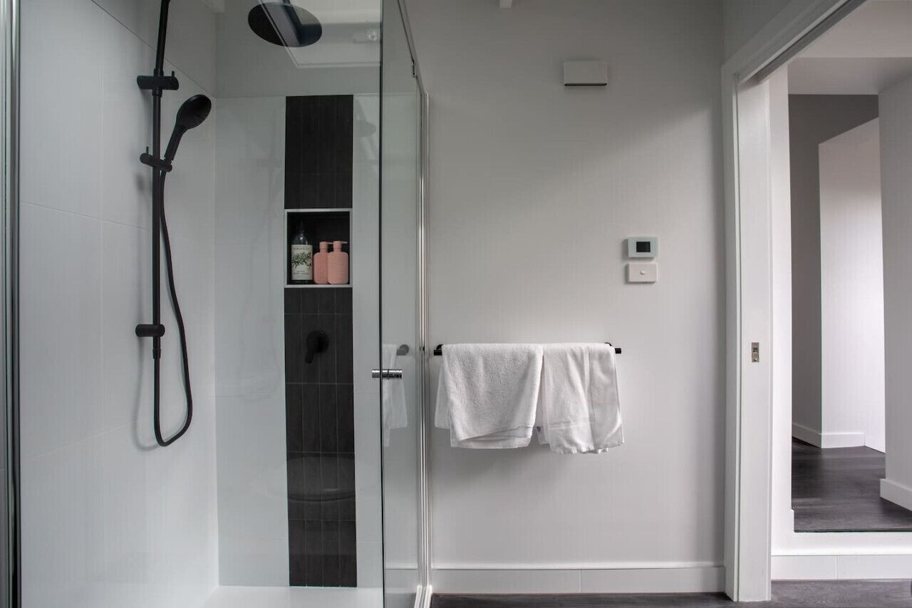 Et moderne badeværelse med en glas brusekabine, et håndklædestativ med to håndklæder og en lille hylde med toiletartikler.