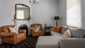 A living room with a fireplace, two leather armchairs, a grey sofa, and a chandelier.